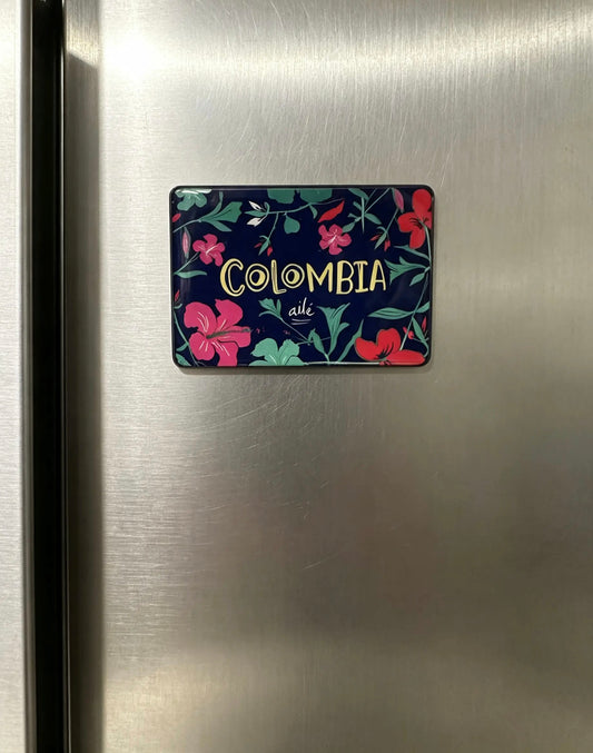 Imán de nevera floral 'Colombia' sobre fondo oscuro, flores rosadas y rojas, imán Colombia floral fondo oscuro, souvenir imán flores colombianas, imán botánico Colombia dorado, diseño floral tropical imán, flores rosadas, colombianas ilustradas, imán vegetación Colombia oscuro, comprar imán floral Colombia, regalo souvenir botánico colombiano, Ailé.
