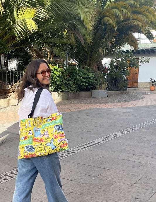 tote bag colombianismos ambiente colonial, souvenir colombiano estilo callejero, bolso amarillo lettering, vegetación tropical, tote bag Colombia entorno colonial, expresiones típicas colombianas, dichos colombianos souvenir, regalo gracioso Colombia, sombrero vueltiao ilustrado, tote bag frases colombianas, bolso colombianismos, tote bag "qué chimba", souvenir con jerga colombiana, bolsa amarilla lettering Colombia, Ailé