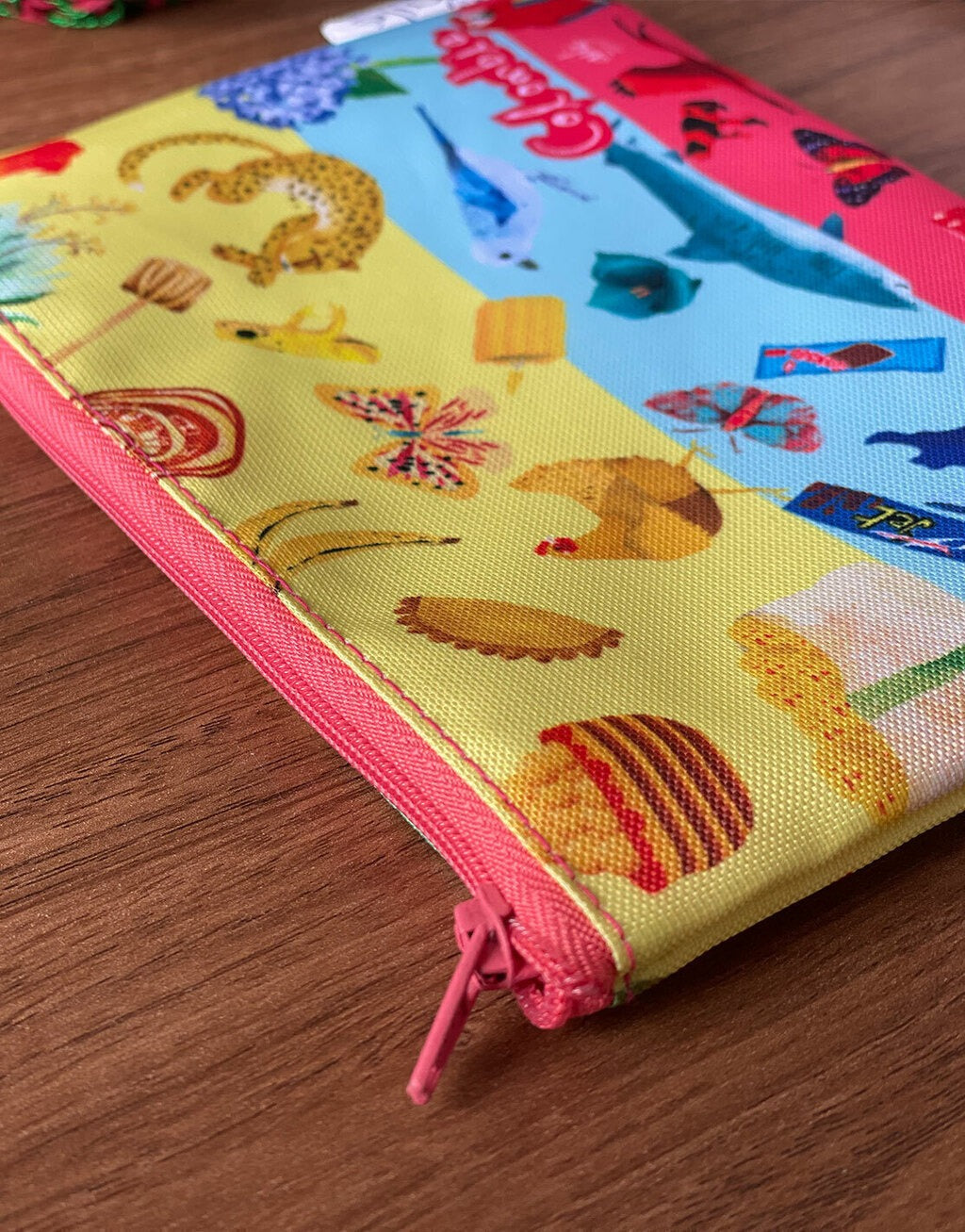 Detalle de cosmetiquera ilustrada con fauna colombiana — jaguar, mariposas, gallina, azulejo, guacamaya roja, corocora y cremallera fucsia — diseño colombiano Ailé