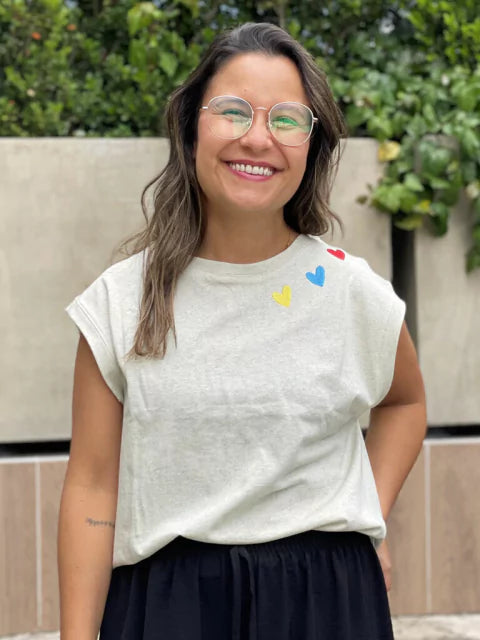 Mujer usando camiseta Ailé con corazones bordados de colores, moda colombiana sostenible, camiseta bordada a mano, camiseta corazones bordados, camiseta gris estampada mujer, camiseta algodón orgánico Colombia, camiseta detalles bordados colores, Colombian design t-shirt, handmade embroidered shirt Colombia, Colombian souvenir clothing, ethical fashion Colombia gift, wearable Colombian art. Ailé