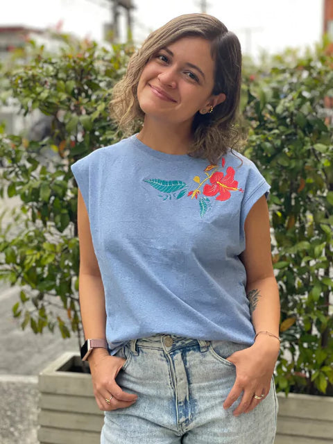 Mujer usando camiseta azul Ailé con bordado floral rojo, moda inspirada en la cayena, camiseta floral mujer Colombia, camiseta bordado flor tropical, camiseta azul estampada flor, camiseta algodón bordado floral, ropa flora colombiana ilustrada, camiseta bordada flor tropical comprar, dónde comprar camiseta floral colombiana, camiseta algodón bordado flor online, marca colombiana ropa floral ilustrada. Ailé