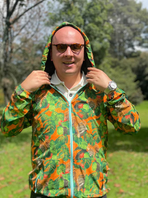 Chaqueta con capota colombiana con diseño jaguares colombianos entre hojas tropicales en naranja y verde, selva, regalo fauna silvestre Colombia, colombian wildlife waterproof jacket, colombian fauna windbreaker gift, eco friendly Colombia jacket design, chaquetas rompevientos institucionales ecológicas, chaqueta rompevientos para regalo cumpleaños, rompevientos para festival de música, chaquetas con diseños de jaguares, chaquetas antifluido de moda colombia, rompevientos liviano de tela reciclada. Ailé