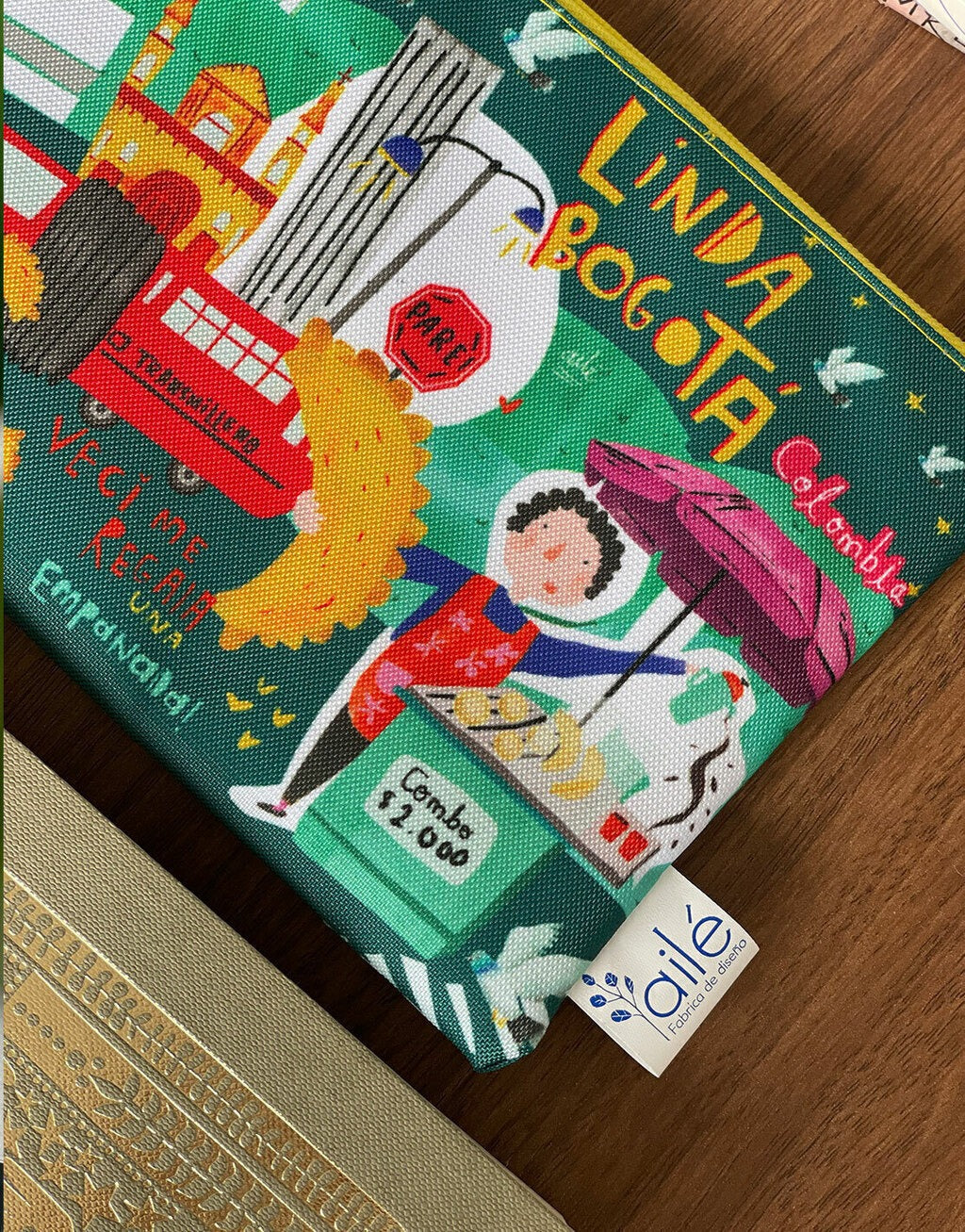 Detalle de cosmetiquera impermeable "Linda Bogotá" con vendedora de empanadas ilustrada, monserrate, torre colpatria, museo del oro, palomas, souvenir bogotano, regalo para extranjeros. Ailé