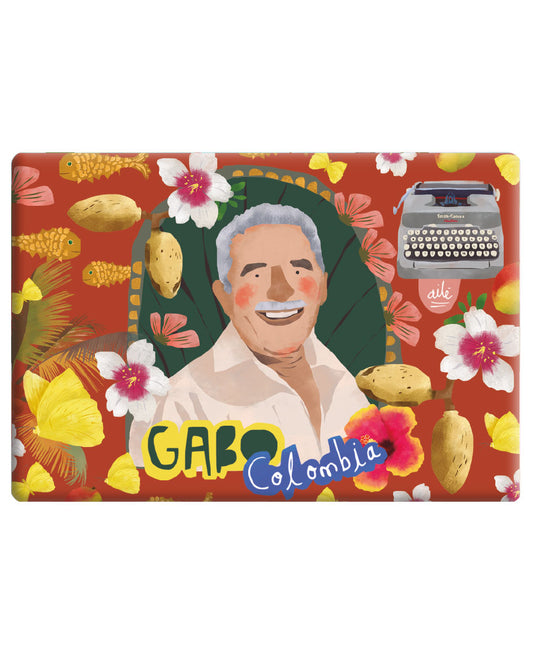 Imán souvenir Colombia ilustrado fondo terracota/rojo oscuro con retrato de Gabriel García Márquez sonriente — rodeado de mariposas amarillas, peces dorados, flores tropicales rosas y blancas, mangos. Máquina de escribir ilustrada en la parte inferior. Gabo Colombia souvenir imán Colombia, recuerdo de Colombia imán, imán biodiversidad colombiana, imán turístico Colombia, Colombian fauna magnet souvenir, imán regalo colombiano, souvenir colombiano imán nevera, imán refrigerador colombiano. Ailé