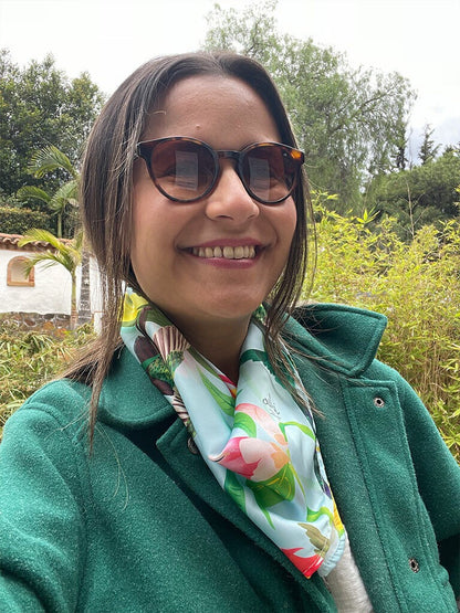 Mujer viajera usando una pañoleta ecológica de cuello con estampado inspirado en los colibríes colombianos, aves emblemáticas de la biodiversidad, Colombia souvenir bandana illustrated, pañoleta decorativa Colombia, bandanas de tela reciclada de plástico. Ailé