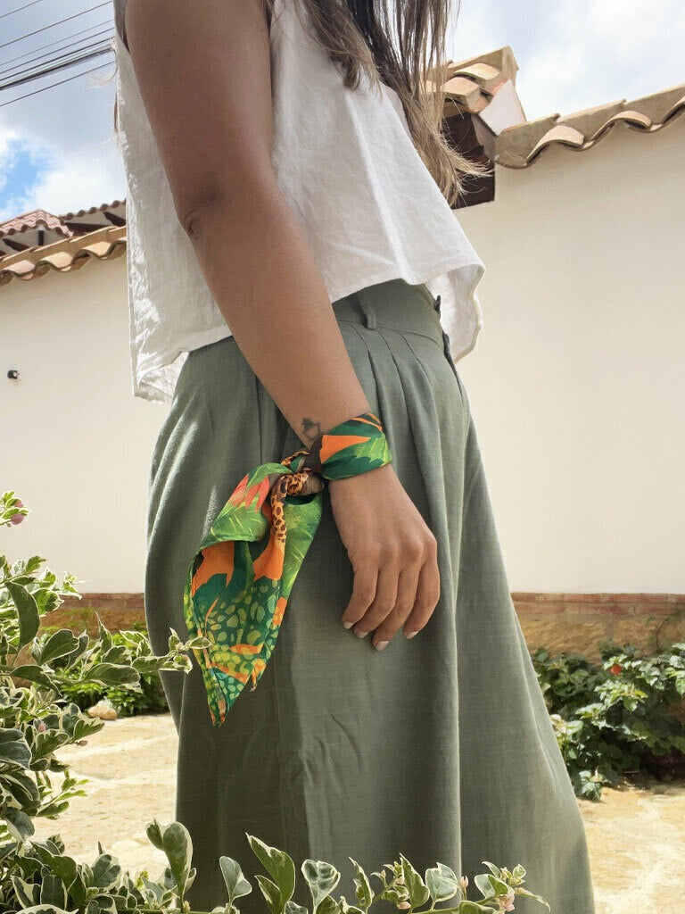 Detalle de pañoleta de tela plástica reciclada amarrada en la muñeca como accesorio de moda selva, regalo fauna silvestre Colombia, souvenir Colombia accesorio viaje pañoleta, pañoleta cabeza Colombia, pañoleta mediana ilustrada Colombia, regalo pañoleta colombiana original, pañoleta multiusos ilustrada, regalo accesorio colombiano ilustrado, accesorio con identidad colombiana, pañoleta playera colombiana, pañoleta amarrada como blusa mujer, complementos de moda para viajeras colombia. Ailé