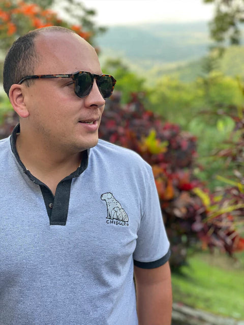 Hombre usando polo gris Ailé con chigüiro bordado, moda inspirada en fauna colombiana, polo hombre chigüiro, polo bordado fauna colombiana, polo algodón diseño animal Colombia, ropa hombre inspirada en Llanos, polo casual bordado animal, chigüiro bordado ropa, ropa fauna llanera colombiana, diseño chigüiro Colombia, chigüiro símbolo colombiano, ropa inspirada en los Llanos Orientales, dónde comprar polo bordado chigüiro, polo chigüiro hecho en Colombia. Ailé