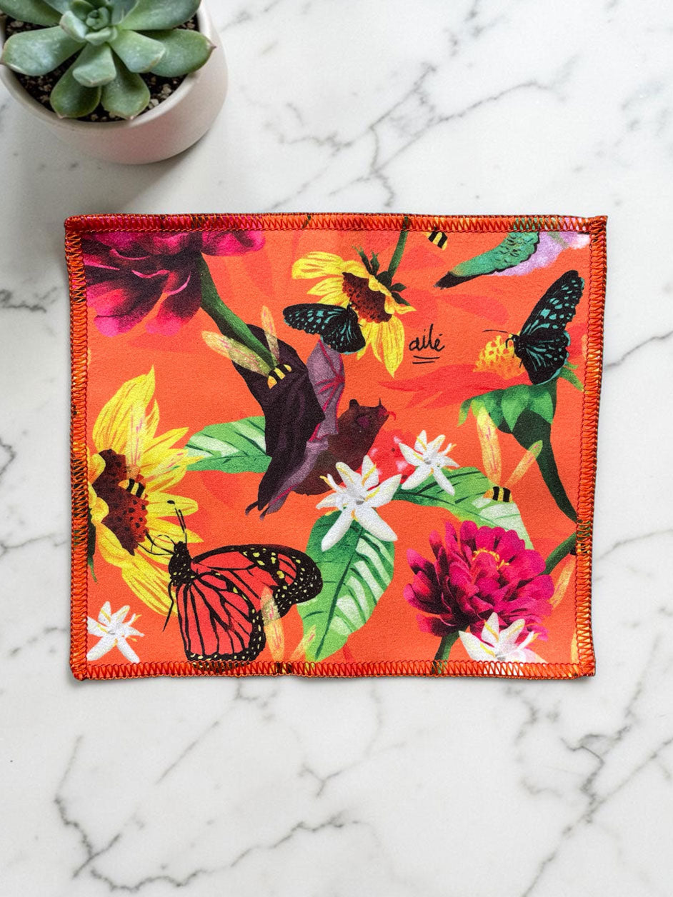 Limpiador pantallas microfibra ilustrado fondo naranja vibrante polinizadores colombianos, mariposa monarca, colibrí, abejas, murciélago, flores grandes fucsia y girasoles amarillos, regalo pequeño colombiano original, regalo ecológico paño Colombia, detalle Amor y Amistad Colombia, toallita tres usos Colombia, limpiapantallas colombiano ilustrado, souvenir Colombia regalo económico, limpiagafas con diseño colombiano, paño microfibra ilustrado Colombia, accesorios ecologicos para el cuidado de lentes. Ailé