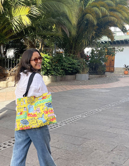 tote bag colombianismos ambiente colonial, souvenir colombiano estilo callejero, bolso amarillo lettering, vegetación tropical, tote bag Colombia entorno colonial, expresiones típicas colombianas, dichos colombianos souvenir, regalo gracioso Colombia, sombrero vueltiao ilustrado, tote bag frases colombianas, bolso colombianismos, tote bag "qué chimba", souvenir con jerga colombiana, bolsa amarilla lettering Colombia, Ailé