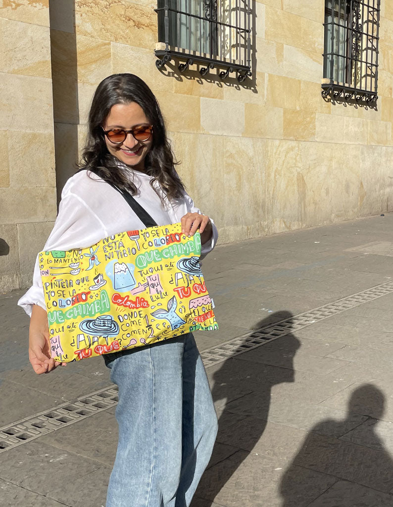 Tote bag amarilla de colombianismos, tote bag colombianismos detalle, 
bolso lettering Colombia de cerca, souvenir "qué chimba" detalle diseño, tote bag amarilla, expresiones típicas colombianas, dichos colombianos souvenir, regalo gracioso Colombia, sombrero vueltiao ilustrado, tote bag frases colombianas, bolso colombianismos, tote bag "qué chimba", souvenir con jerga colombiana, bolsa amarilla lettering Colombia, Ailé.